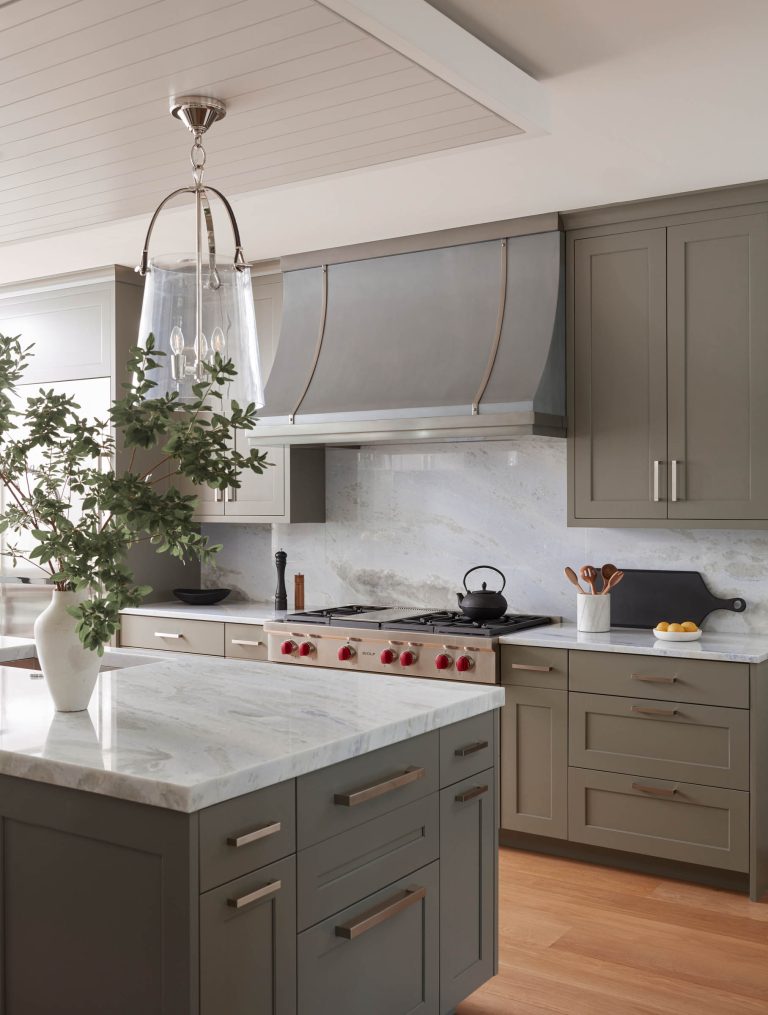 Modern kitchen with sage green cabinets, marble countertops, and backsplash. Designed by interior designer Glenna Stone and located on the Main Line, it features a spacious island, stainless appliances with red knobs, and light wood floors.