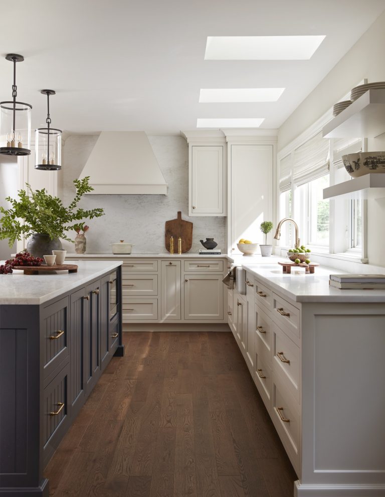 Bright, modern kitchen with white cabinets, marble counters, and a dark wood island designed by Main Line decorator Glenna Stone. Large windows and skylights fill the space with light in this Penn Valley home. Plants and artful decor accent the wooden floors throughout.